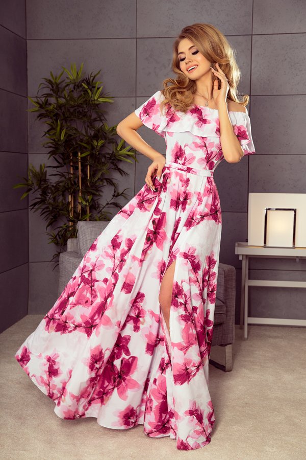 A woman is wearing an elegant, off-the-shoulder dress adorned with vibrant pink floral patterns. The dress features a flowing skirt with a stylish slit, perfect for a sophisticated and feminine look.