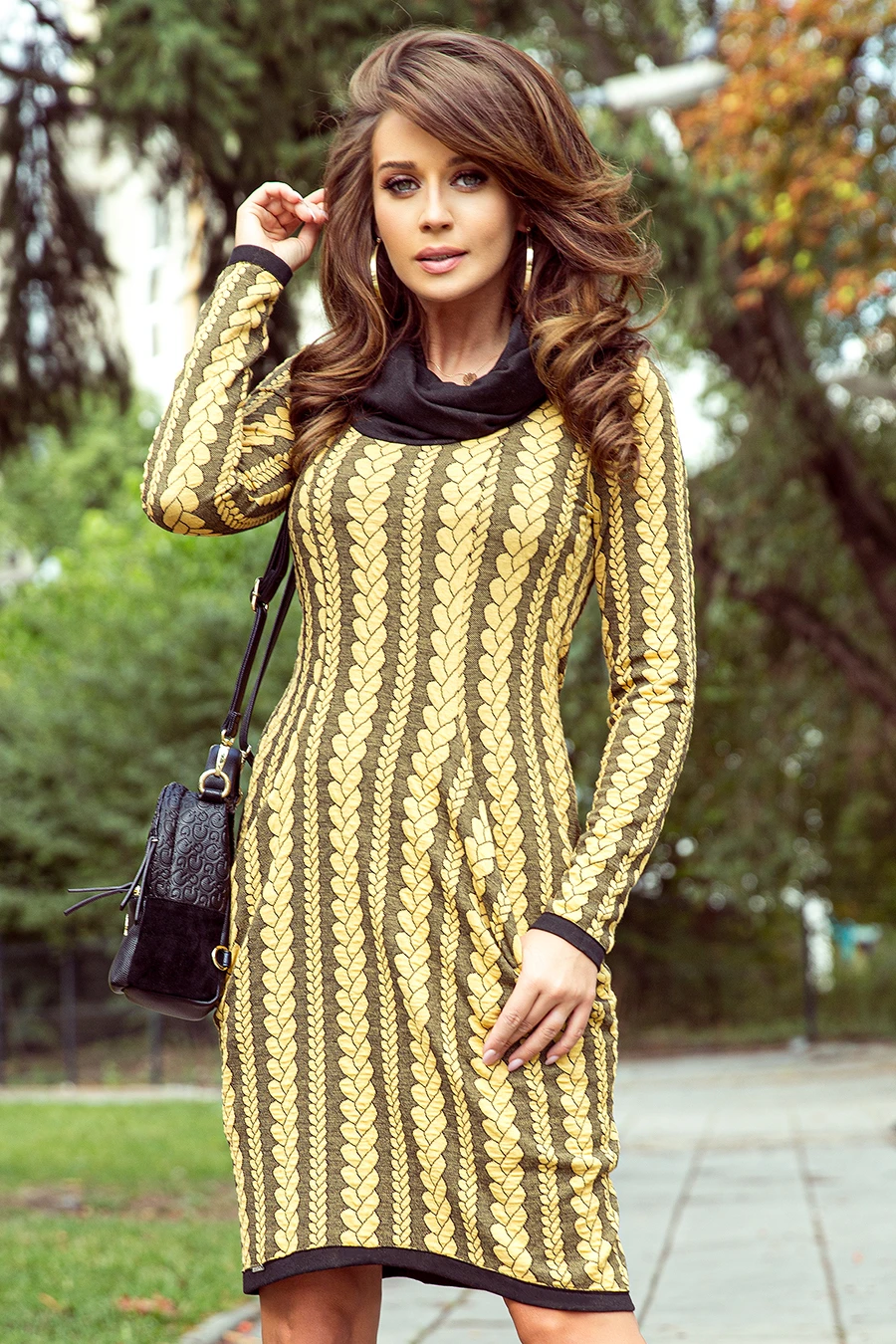 A stylish dress featuring a bold, golden leaf pattern on a dark background, complemented by a black collar and cuffs. The outfit is paired with a chic black handbag, adding a touch of elegance to the ensemble.