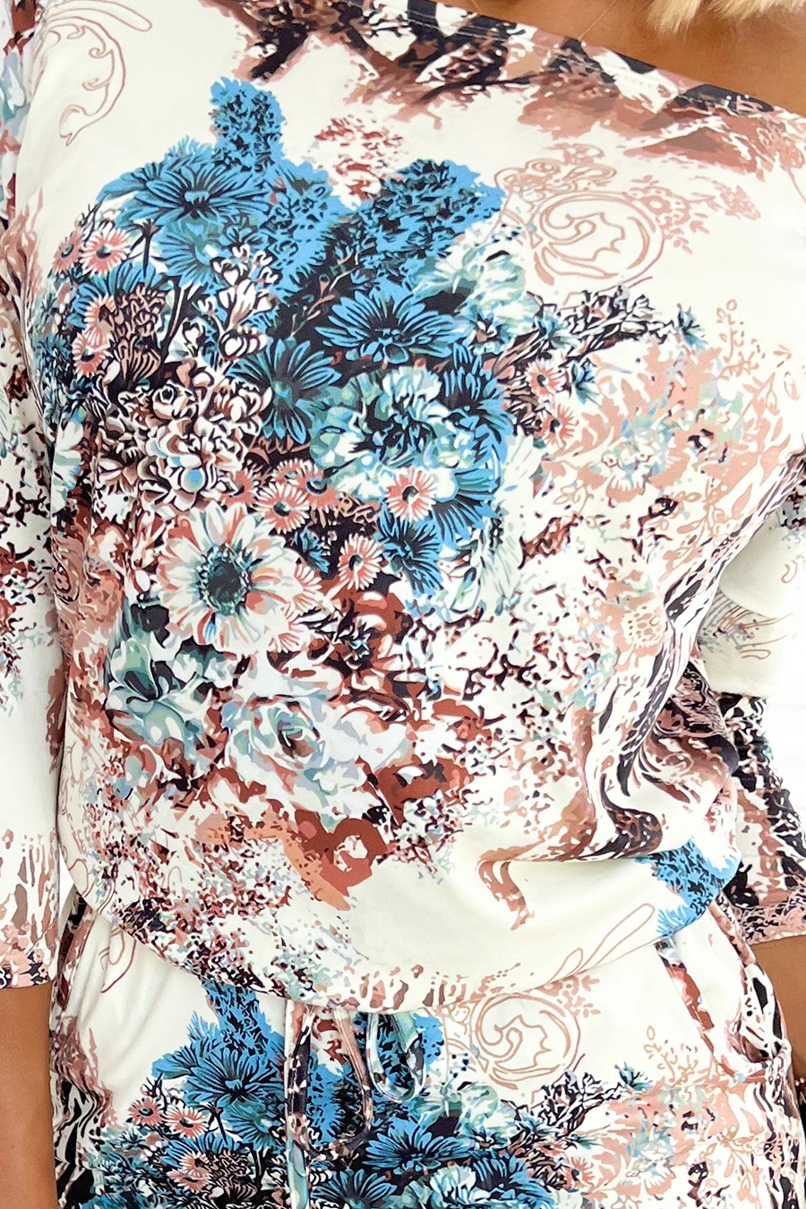 The image showcases a dress featuring a vibrant floral pattern in shades of blue, pink, and brown on a light background. The design includes intricate details that create a dynamic and eye-catching look.