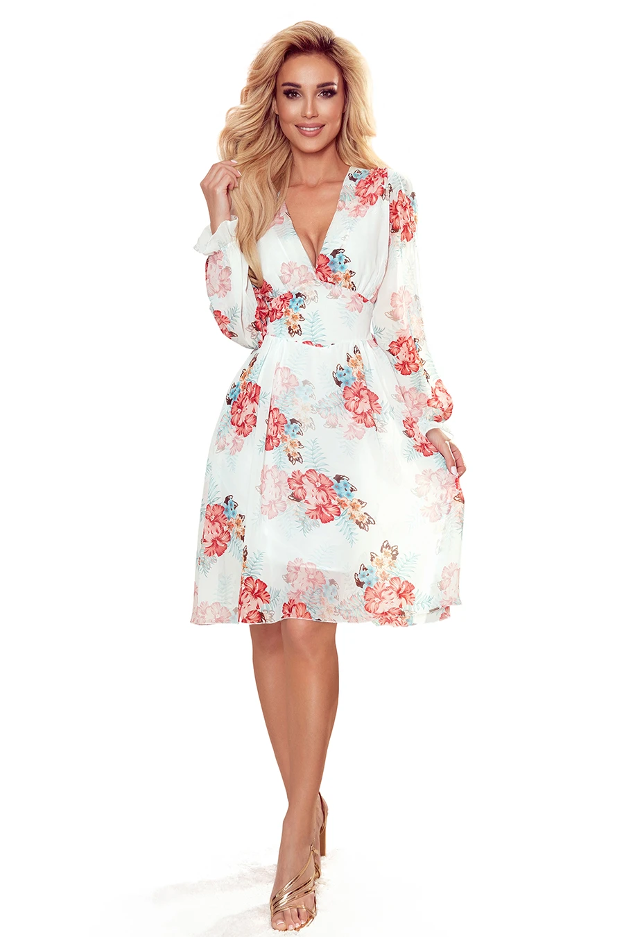 A woman is wearing a light, floral-patterned dress with long sleeves and a V-neckline. The dress features a mix of red, pink, and blue flowers on a white background, creating a fresh and elegant look.