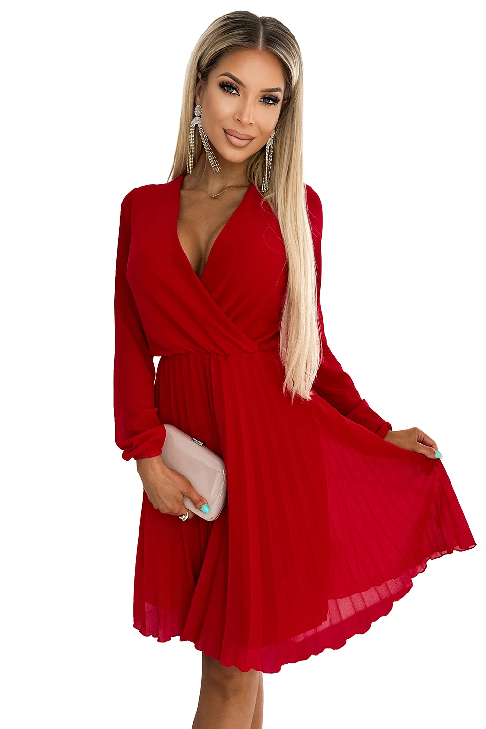 A woman is wearing a vibrant red dress with a pleated skirt and a deep V-neckline. She holds a beige clutch, complementing the elegant and stylish look.