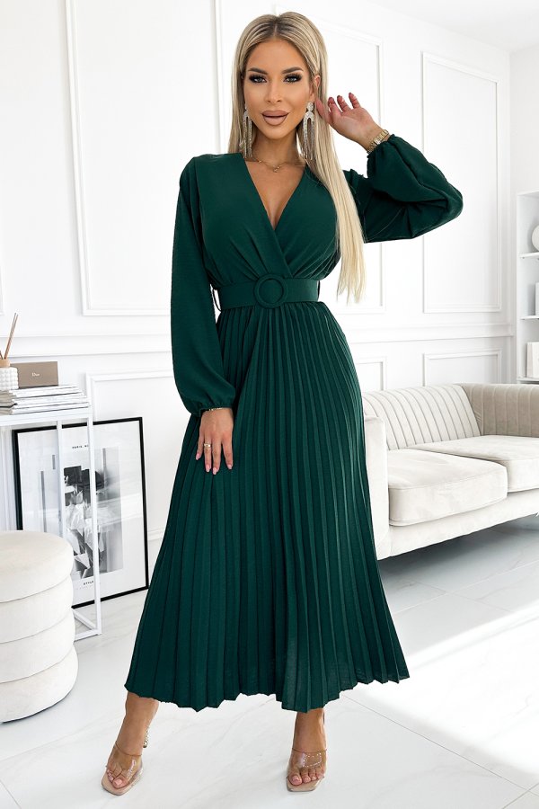 A woman is wearing an elegant, deep green pleated dress with a V-neckline and a matching belt. The dress features long sleeves and a flowing skirt, perfect for a sophisticated look.