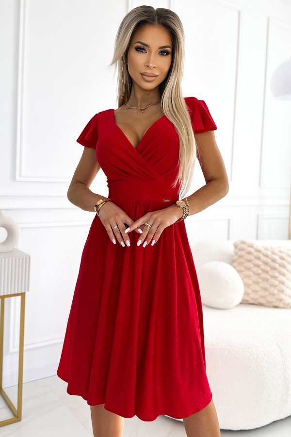 A woman is wearing a vibrant red dress with a fitted bodice and a flared skirt, perfect for elegant occasions. The dress features short sleeves and a flattering V-neckline, adding a touch of sophistication.