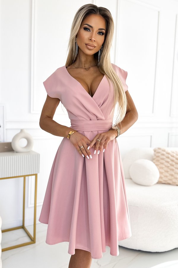 A woman is wearing an elegant pink dress with a fitted waist and a flared skirt. The dress features a deep V-neckline and cap sleeves, creating a sophisticated and stylish look.