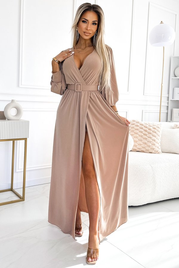 A stylish, long beige dress with a deep V-neckline and a matching belt accentuates elegance and sophistication. The dress features a high slit, adding a touch of allure to the overall design.