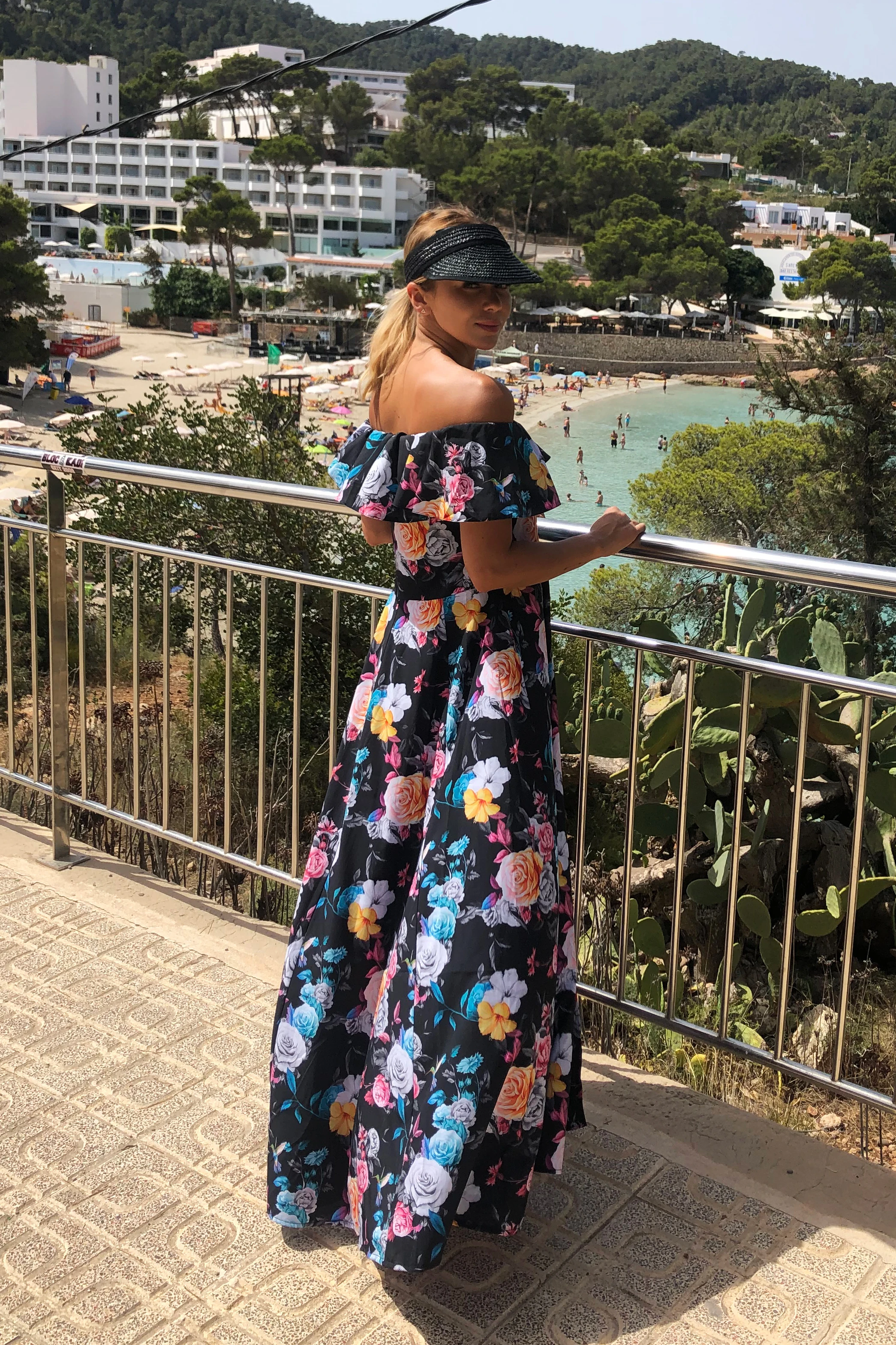 A woman is wearing a long, off-the-shoulder dress with a vibrant floral pattern, perfect for a summer outing. The dress features a flowing design with colorful flowers on a dark background, creating a striking contrast.