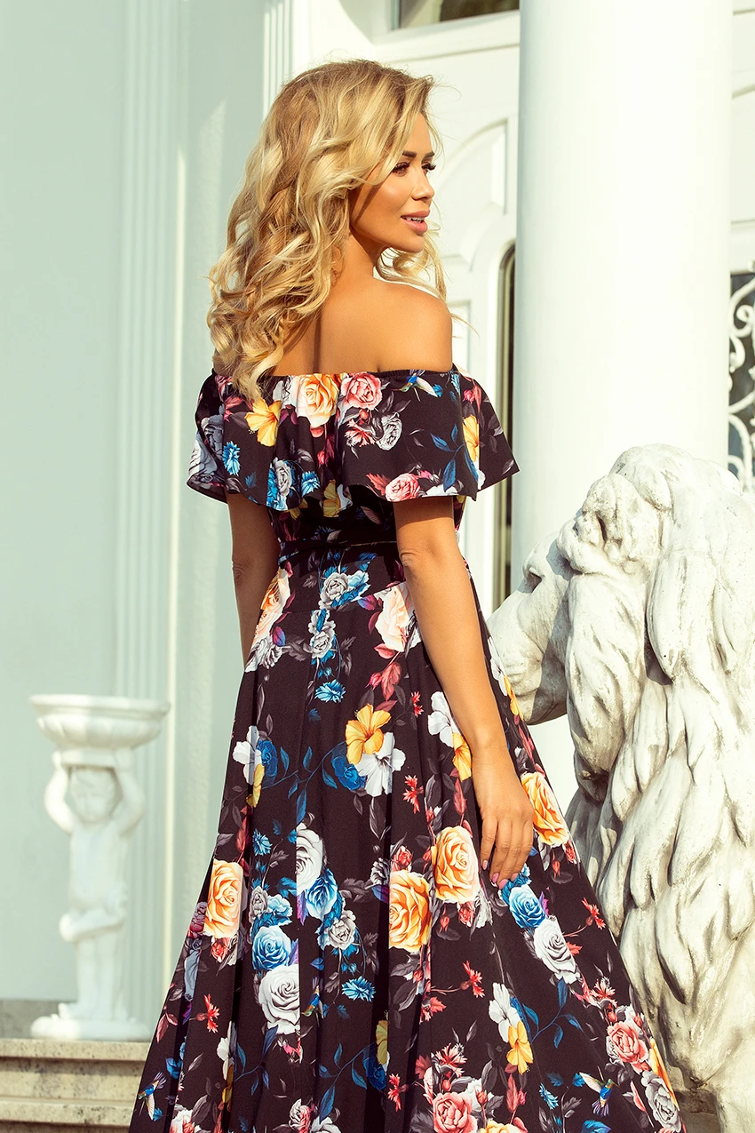 A woman is wearing an elegant off-the-shoulder dress adorned with a vibrant floral pattern. The dress features a flowing design, perfect for a stylish and sophisticated look.