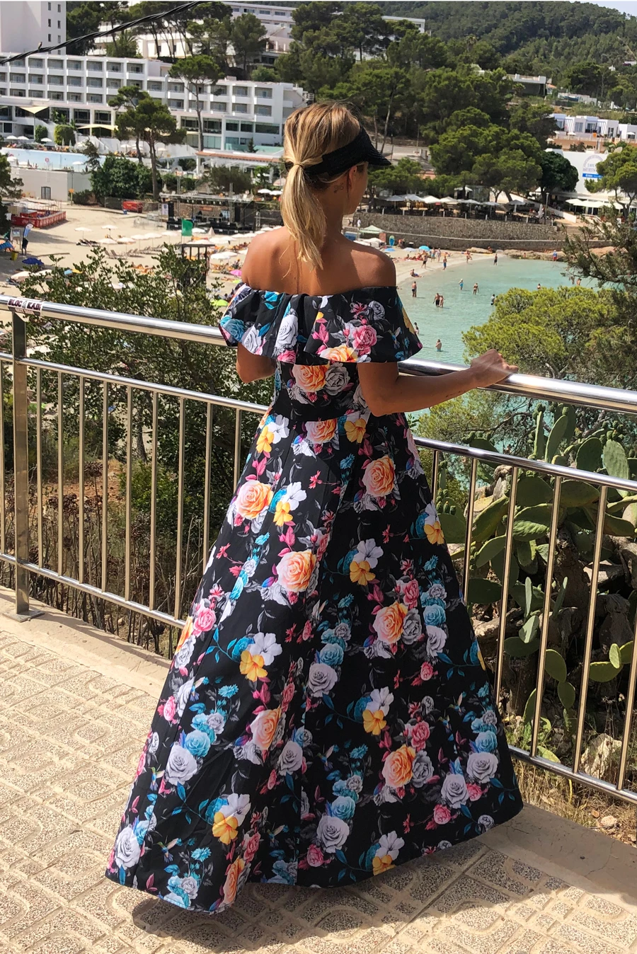 A woman is wearing a long, off-the-shoulder dress with a vibrant floral pattern. The dress features a flowing design, perfect for a summer outing.