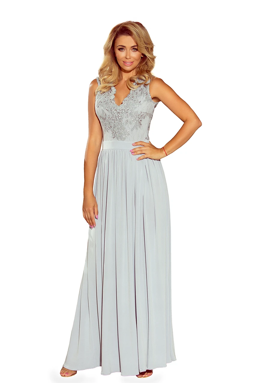A long, elegant evening gown in a soft, light gray color features intricate lace detailing on the bodice. The dress has a flowing skirt that adds a touch of sophistication and grace.