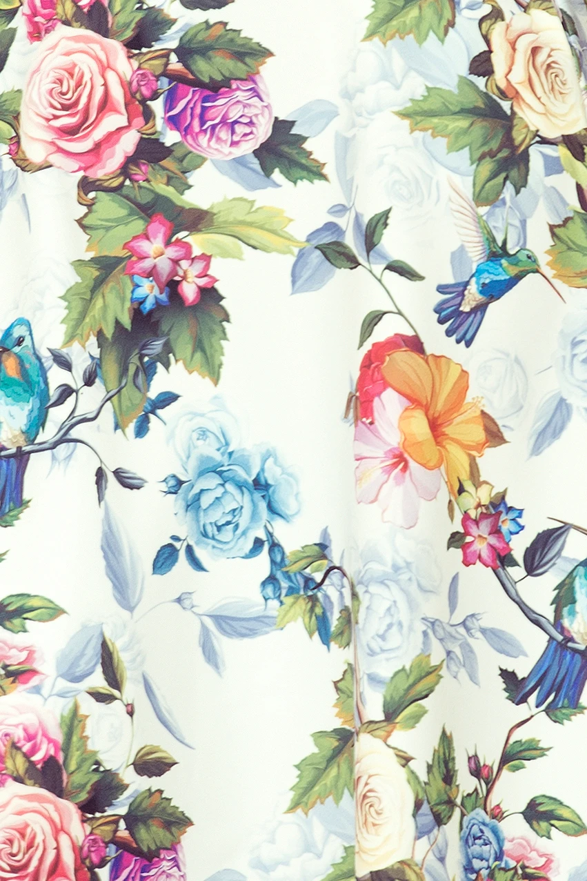 The image showcases a vibrant fabric with a floral and bird pattern, featuring roses and hummingbirds in a variety of colors. The design is set against a light background, creating a fresh and lively appearance.