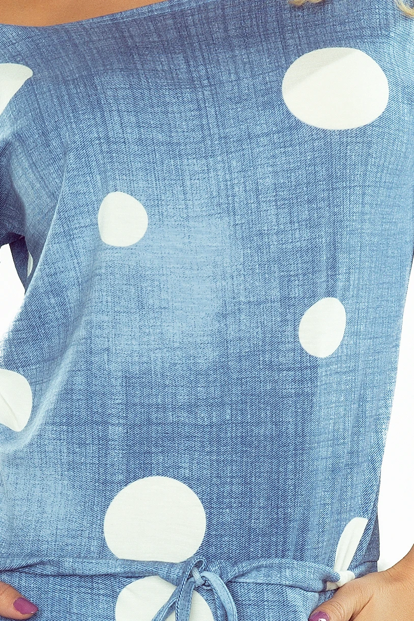 The image shows a blue dress with a white polka dot pattern and a tie at the waist. The fabric has a textured appearance, adding a stylish touch to the design.