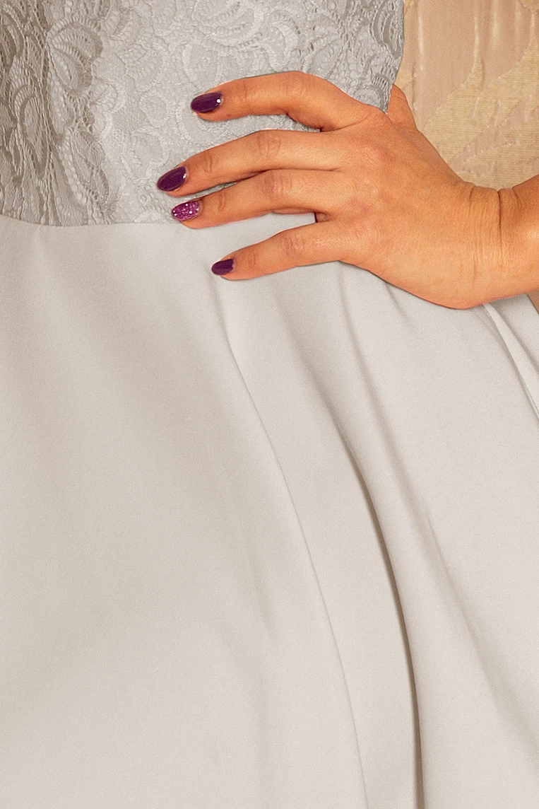 The image shows a close-up of a dress featuring a delicate lace bodice and a smooth, flowing skirt. The fabric appears elegant and is complemented by a hand with purple nail polish resting gently on the waist.