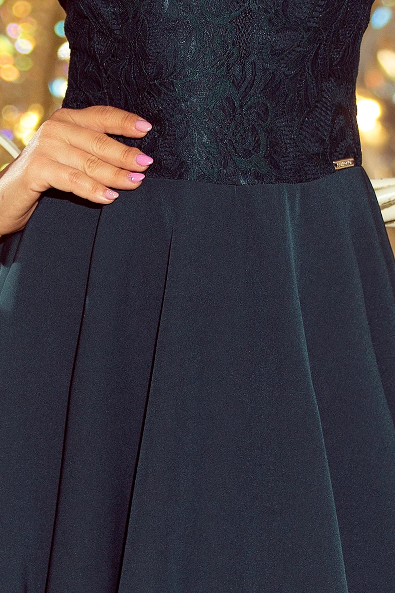 A dark, elegant dress features a textured lace bodice and a flowing skirt. The design is complemented by a subtle metallic detail at the waist.