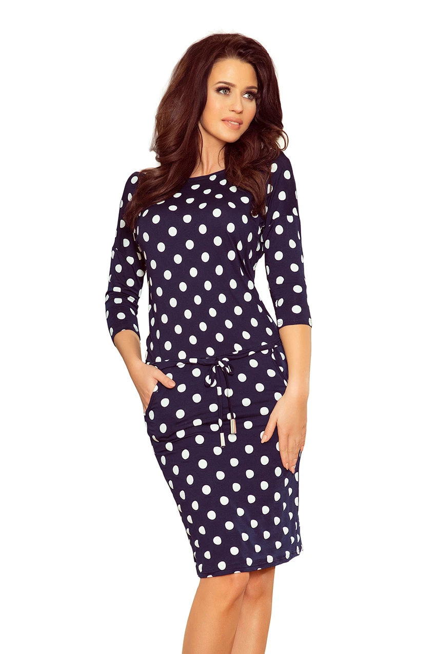 A navy blue dress with white polka dots features a fitted silhouette and three-quarter sleeves. The dress includes a drawstring waist for added style and comfort.