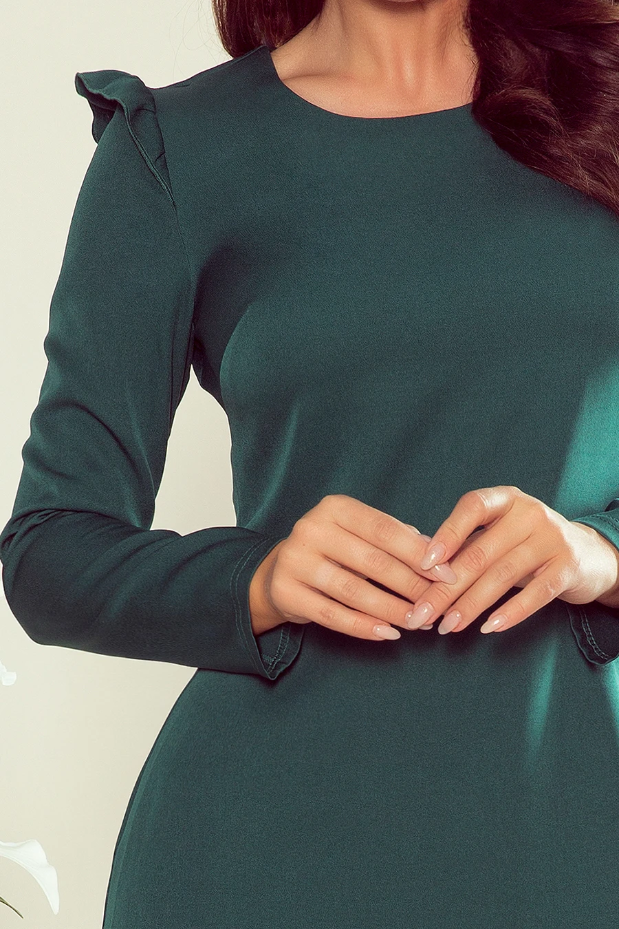 The image features a woman wearing an elegant, dark green dress with long sleeves and subtle ruffle details on the shoulders. The fabric appears smooth and fitted, highlighting a sophisticated and stylish design.