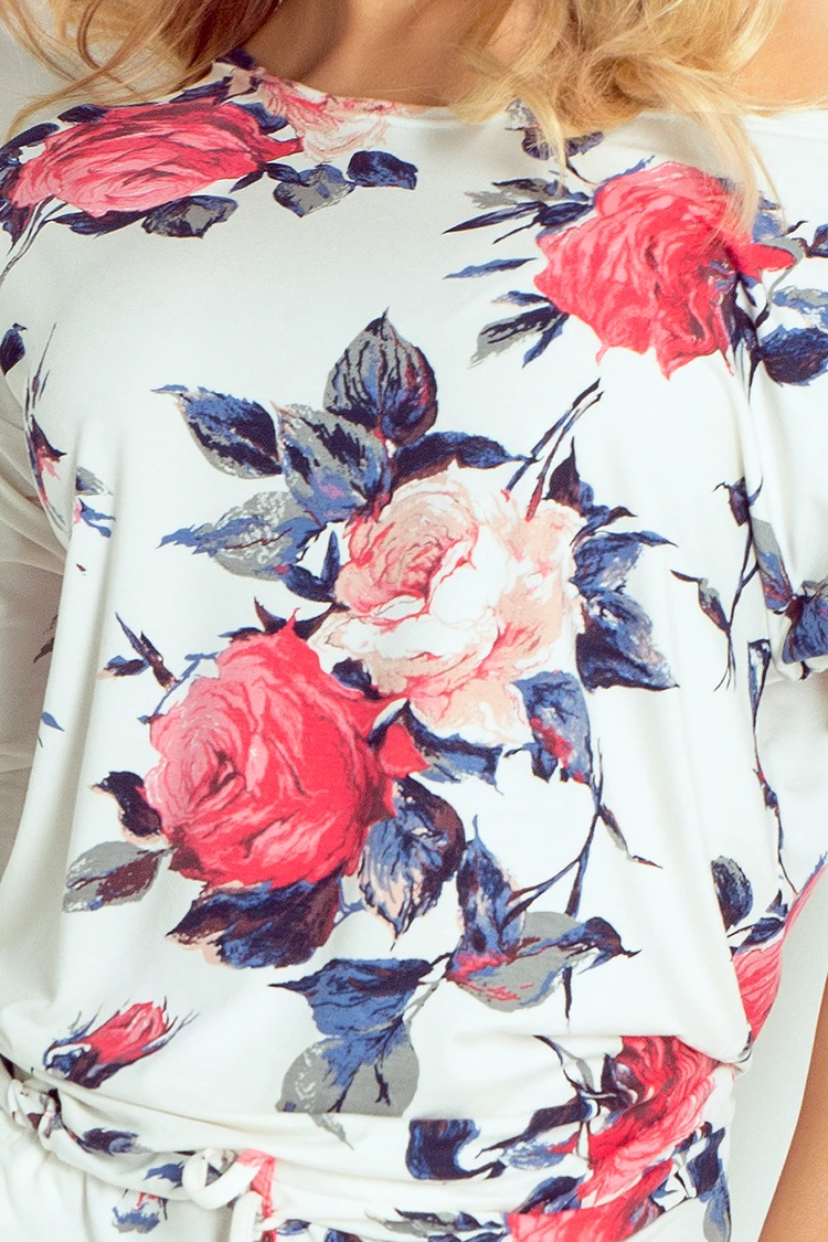 A white garment featuring a vibrant floral pattern with red and pink roses and blue leaves. The fabric appears soft and comfortable, ideal for a stylish and elegant look.