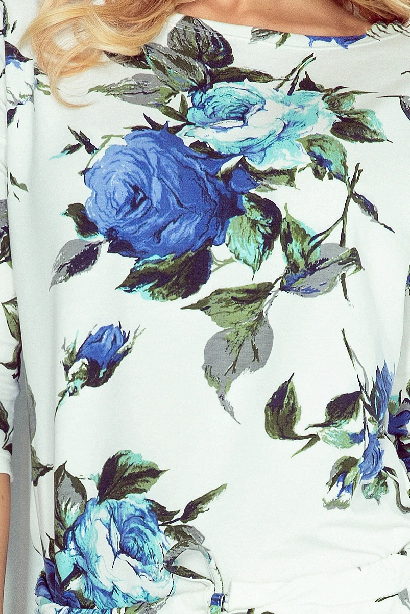 A white garment featuring a vibrant blue floral pattern with green leaves. The design is elegant and eye-catching, perfect for adding a touch of color to any outfit.
