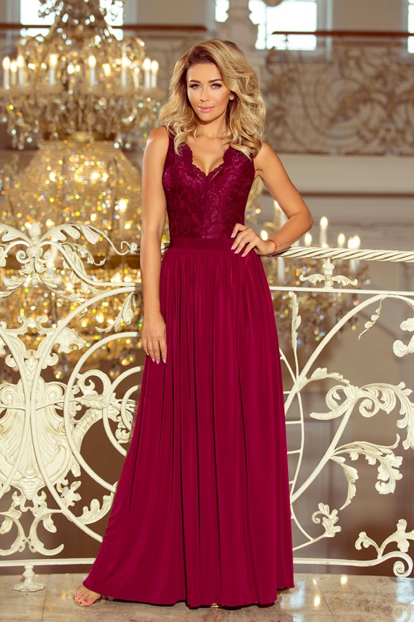 A woman is wearing an elegant, floor-length burgundy gown with a lace bodice and flowing skirt. The dress is showcased in a luxurious setting with ornate chandeliers in the background.