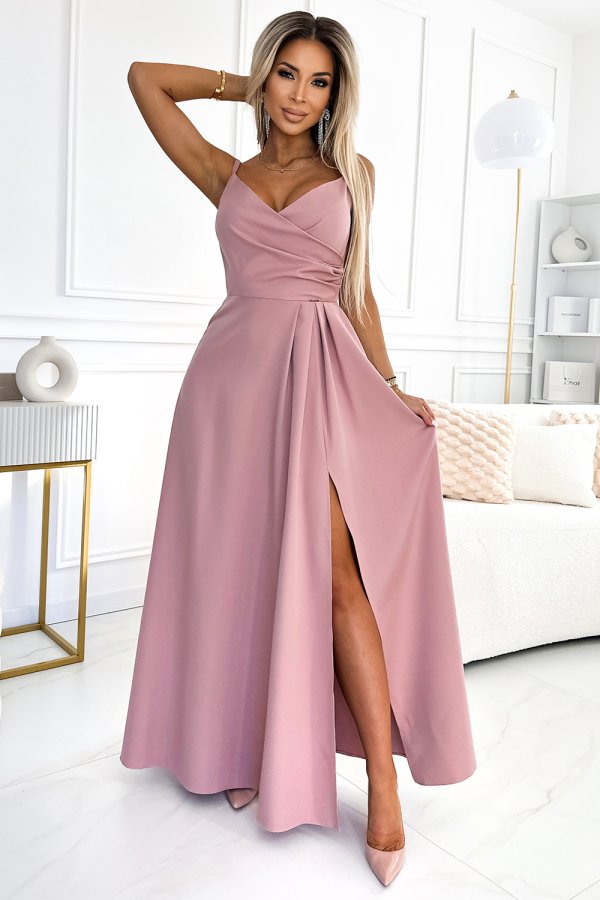 A woman is wearing an elegant, floor-length pink dress with a wrap-style bodice and a high slit. The dress is complemented by matching pink heels, creating a sophisticated and stylish look.