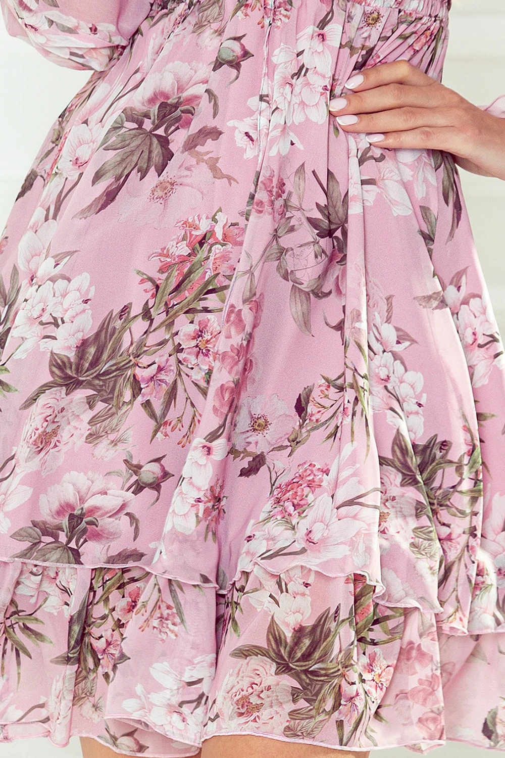 A pink floral dress with a delicate pattern of blooming flowers and green leaves. The fabric is lightweight and features a layered, ruffled hem for a feminine touch.