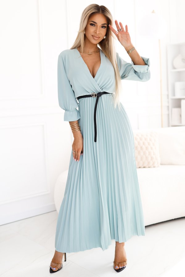 A light blue, pleated maxi dress with a deep V-neckline and three-quarter sleeves is elegantly cinched at the waist with a slim black belt. The dress exudes a sophisticated and airy style, perfect for both casual and formal occasions.