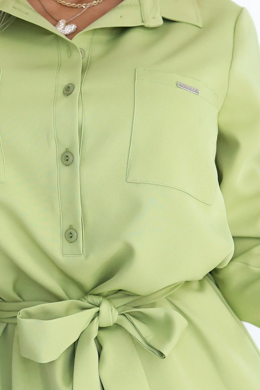 A light green shirt dress features a button-up front and a stylish waist tie. The design includes two chest pockets for added detail.