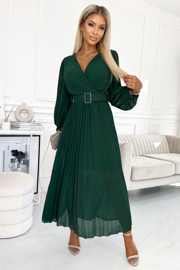The woman in the photo is wearing an elegant green pleated dress, perfect for formal occasions. The dress features a stylish belt that accentuates the waist, highlighting the sophisticated design.