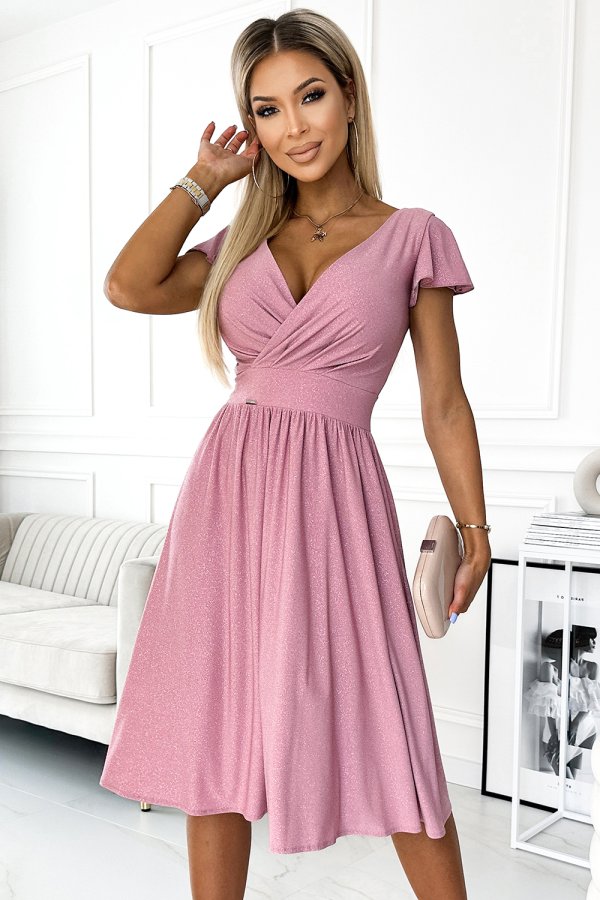 A woman is wearing a stylish pink dress with a flattering V-neck and short sleeves. The dress features a fitted waist and a flowing skirt, perfect for elegant occasions.