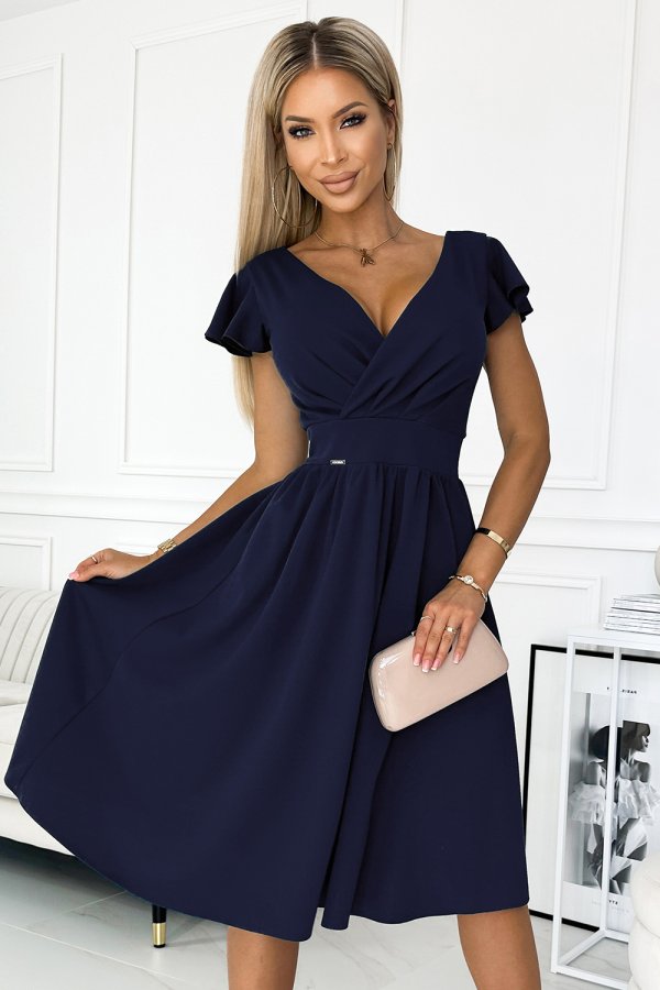 A woman is wearing a stylish navy blue dress with a flattering V-neck and short sleeves. She holds a sleek beige clutch, complementing the elegant look.