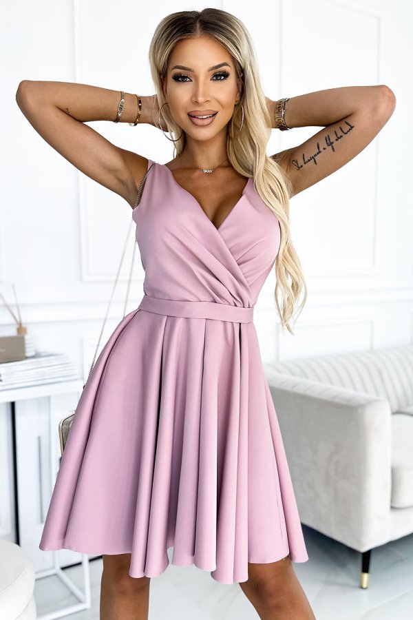 A woman is wearing a sleeveless, light pink dress with a fitted waist and a flared skirt. The dress features a V-neckline and a smooth, elegant fabric, perfect for a stylish and feminine look.