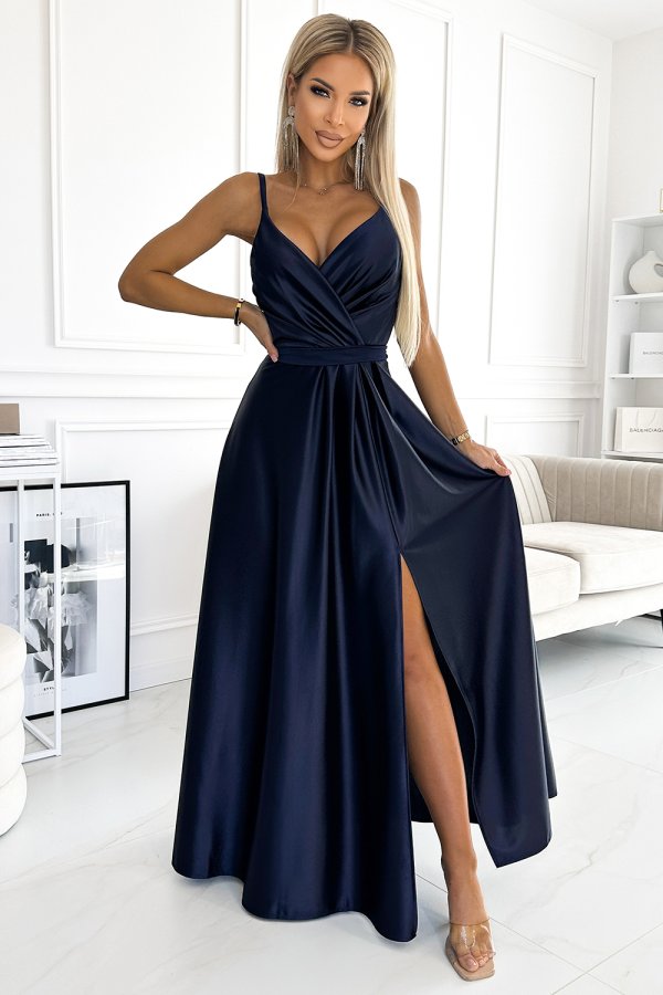 A navy blue evening gown with a deep V-neckline and a high slit, elegantly drapes to the floor. The dress features thin straps and a fitted waist, creating a sophisticated silhouette.